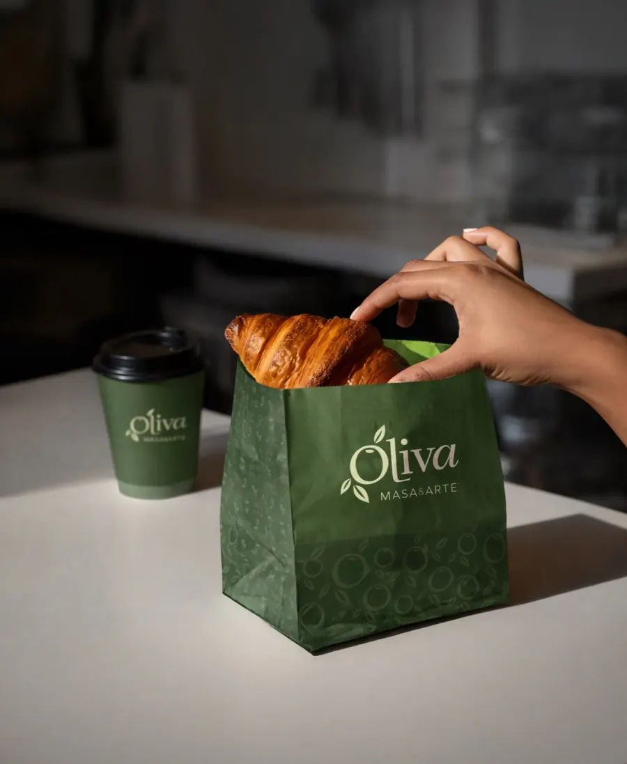 Mano tomando un croissant de una bolsa verde de Oliva.